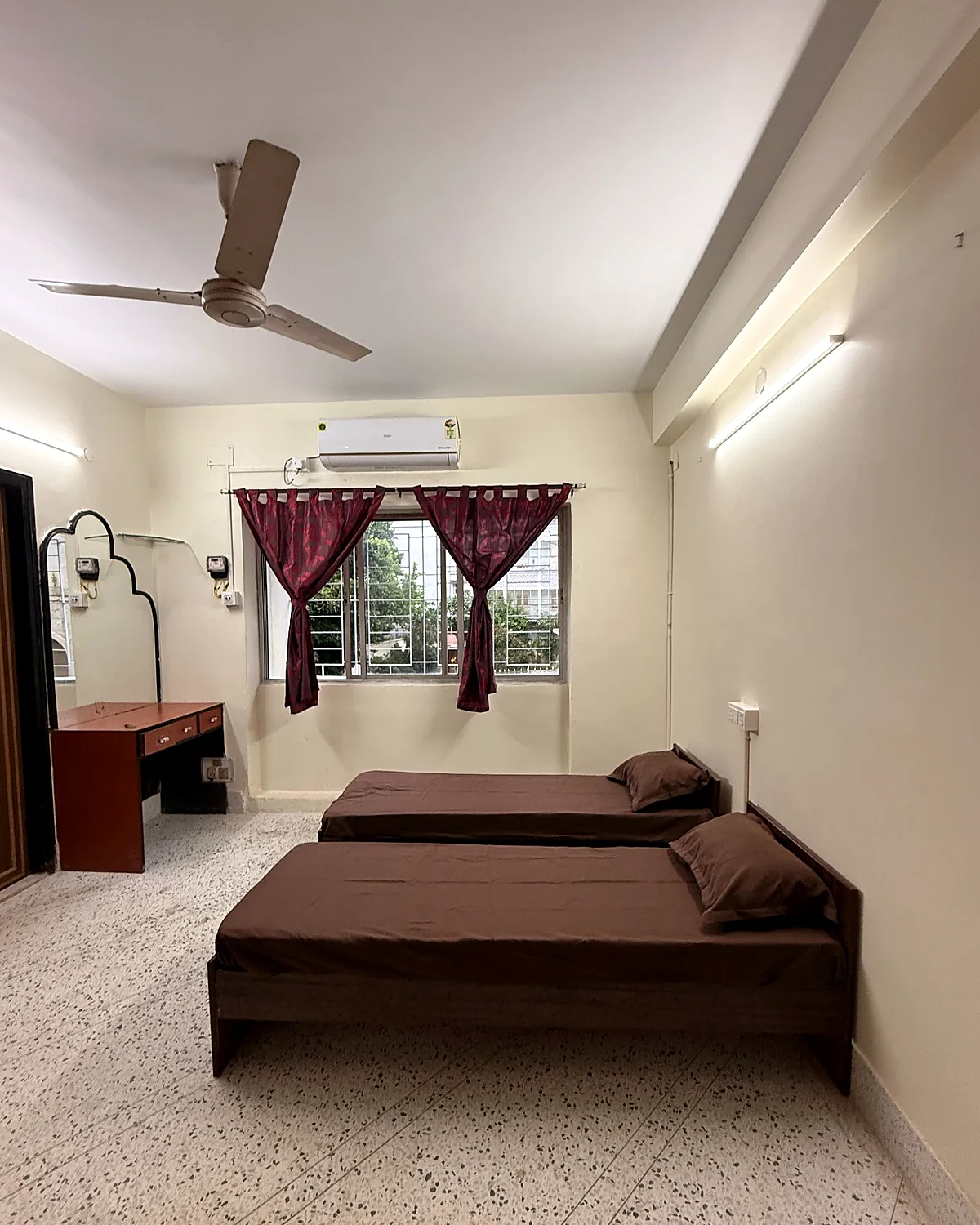 Spacious twin-sharing room at Snehmili Girls PG with two beds, study desk, window and air conditioning
